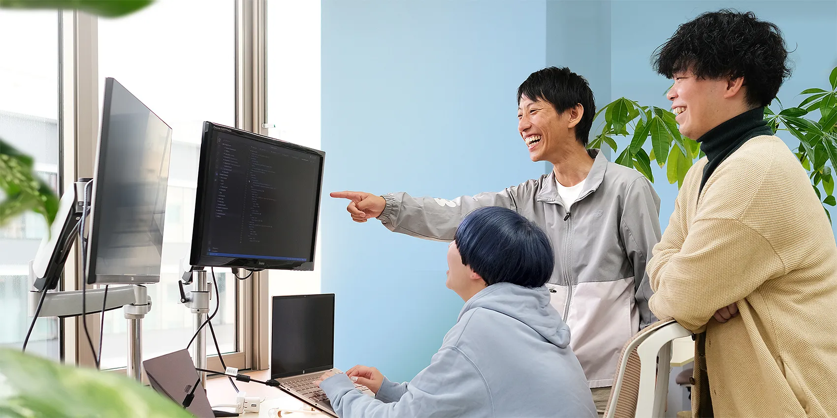 写真　モニターを見ながら社員三名が談笑しつつ相談する様子